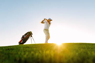 Low angle shot of male golfer taking shot while standing on field. full length of golf player swinging golf club on sunny day. - JLPSF27854