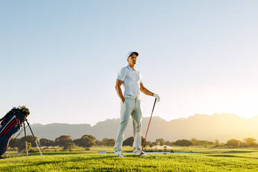 Männlicher Golfer in voller Länge auf dem Golfplatz, der auf den Abschlag wartet, Mann spielt Golf auf einem Feld an einem sonnigen Tag. - JLPSF27855