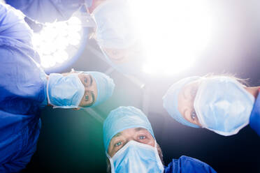 Team of doctors looking down at patient in operation room. Surgeons performing dental surgery. - JLPSF27870