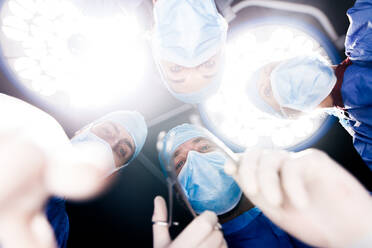 Low angle view of surgeons under surgery lights in operating theatre. Medicine professionals performing dental surgery. - JLPSF27871