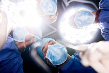 Team of doctors operating under surgery lights in operation theater. Point of view shot of surgeons performing dental surgery in hospital. - JLPSF27873