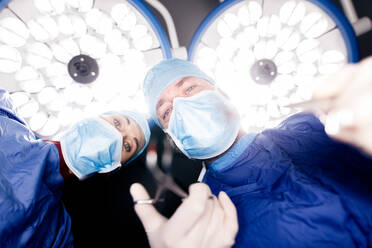 Team of surgeons operating patient under surgery lights in hospital. Doctors performing dental surgery. - JLPSF27875