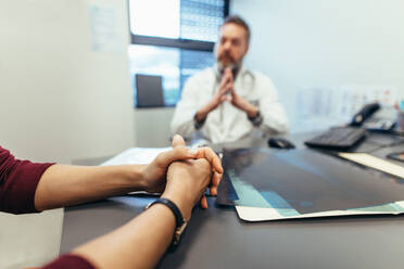 Weibliche Patientin beim Arztbesuch. Frau sitzt am Tisch in der Klinik mit Arzt im Hintergrund. - JLPSF27881