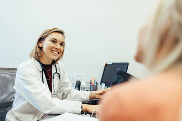 Eine Ärztin hört ihrem Patienten während einer Konsultation in der Praxis zu. Ein Mediziner sitzt an seinem Schreibtisch und berät den Patienten. - JLPSF27886