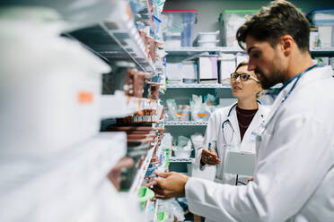 Two pharmacist working in drugstore. Male and female pharmacists checking medicines inventory at hospital pharmacy. - JLPSF27909