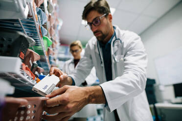 Pharmacist looking for a drug on shelf. Male pharmacist checking stock in an shelf. Medical staff working in hospital pharmacy. - JLPSF27912