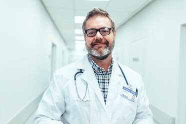 Porträt eines glücklichen reifen männlichen Arztes, der in einem Krankenhauskorridor steht. Kaukasischer Mann, der im Gesundheitszentrum arbeitet. - JLPSF27916