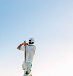 Professioneller Golfer bei einem Schlag gegen den klaren Himmel. Rückansicht eines Golfspielers, der an einem sonnigen Tag den Golfschläger schwingt. - JLPSF27928