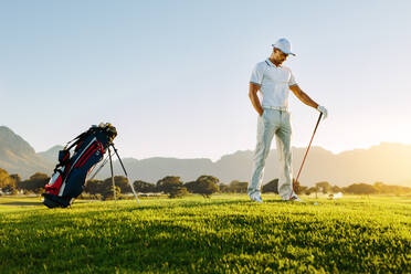 Junger Mann in voller Länge auf einem Golfplatz bei Sonnenuntergang, männlicher Profigolfer mit Golfschläger in der Hand. - JLPSF27933
