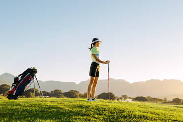 Junge kaukasische Frau steht an einem Sommertag auf einem Golfplatz und hält einen Golfschläger in der Hand. - JLPSF27935