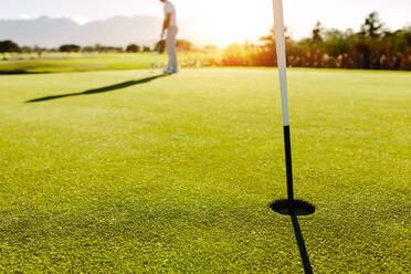 Golfloch und Flagge im grünen Feld mit Golfer im Hintergrund. Professioneller Golfer, der den Ball schlägt. - JLPSF27945