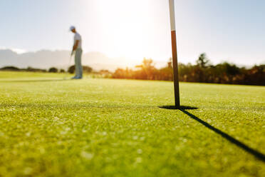 Golfloch und Flagge im grünen Feld mit Golfer im Hintergrund. Professioneller Golfer, der den Ball schlägt. - JLPSF27946