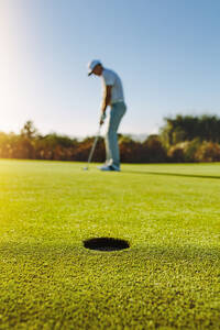 Vertikaler Schuss von Golf-Loch im grünen Feld mit Golfer im Hintergrund. Golf-Spieler Putting Ball in Loch. - JLPSF27948