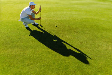 Pro Golfspieler, der mit einem Schläger auf dem Golfplatz zielt. Männlicher Golfer, der die Linie für das Setzen des Golfballs auf grünem Gras überprüft. - JLPSF27958