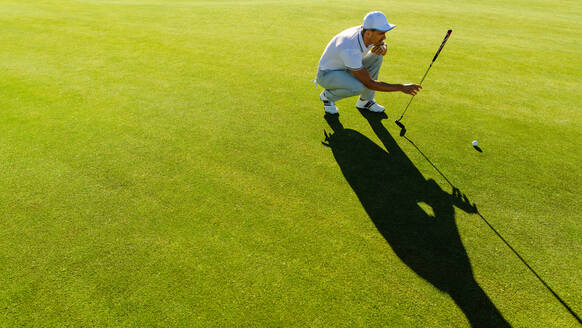 Professioneller Golfer überprüft die Linie für das Putten des Golfballs auf grünem Gras. Golfspieler hockt und studiert das Grün vor dem Putten - JLPSF27959