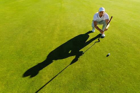 Golfspieler, der mit seinem Schläger auf dem Golfplatz zielt. Männlicher Golfer, der die Linie für das Setzen des Golfballs auf grünem Gras überprüft. - JLPSF27960