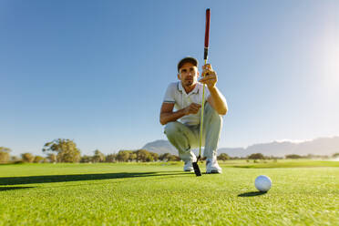 Profigolfer, der mit seinem Schläger auf dem Golfplatz einen Schlag anvisiert. Golfer, der sich hinhockt und das Grün vor dem Putten studiert - JLPSF27961