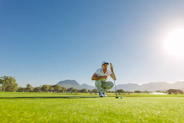 Junger Golfspieler, der seinen nächsten Putt perfekt machen will. Männlicher Golfer, der die Linie für das Putten des Golfballs auf grünem Gras überprüft. - JLPSF27963