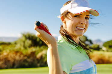 Close up portrait of happy female golfer holding golf club on field. Beautiful young woman standing on golf course and smiling. - JLPSF27981