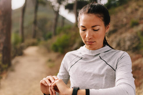 Läuferin, die eine Fitness-App nutzt, um ihre Trainingsleistung zu überwachen, während sie im Freien auf einer Landstraße steht. - JLPSF27985