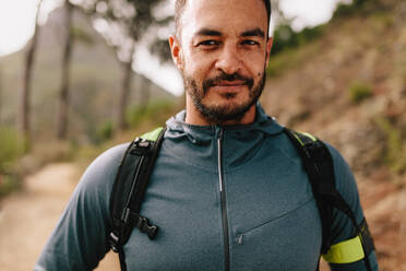 Junger Mann in Sportkleidung auf einem Waldweg stehend und in die Kamera blickend. Fitness-Mann beim Training im Freien. - JLPSF27989