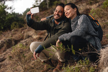 Couple in love sitting on mountain trail and taking selfie. Young man and woman hiking in countryside and talking self portrait with mobile phone. - JLPSF28005