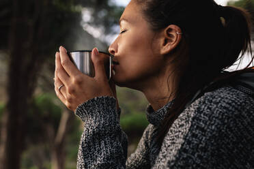 Nahaufnahme einer jungen asiatischen Frau, die im Freien Kaffee trinkt. Eine Wanderin, die sich ausruht und frischen Kaffee trinkt. - JLPSF28010