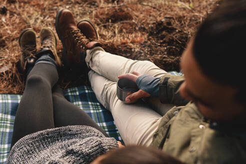 Nahaufnahme eines jungen Paares, das im Freien zusammensitzt, Fokus auf die Hände, die eine Tasse Kaffee halten. Wanderer, die sich am Berghang entspannen. - JLPSF28014