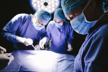 Chirurg mit medizinischer Maske und medizinischem Team bei einer Operation im Operationssaal. - JLPSF28025