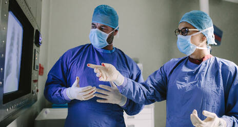 Two surgeons looking at screen and discussing while performing surgery in hospital operating room. Professional medics during surgery in operation theater. - JLPSF28033