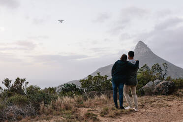 Außenaufnahme eines jungen Paares, das zusammen in der Natur steht und eine Drohne mit einer Fernsteuerung fliegt. - JLPSF28035