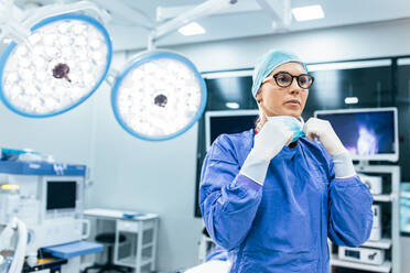 Chirurgin mit chirurgischer Maske im Operationssaal. Junge Ärztin in chirurgischer Uniform im Operationssaal eines Krankenhauses. - JLPSF28042