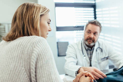 Frau, die über ihre Gesundheit spricht, während der Arzt zuhört. Weibliche Patientin im Gespräch mit dem Arzt während einer Konsultation in der Klinik. - JLPSF28048