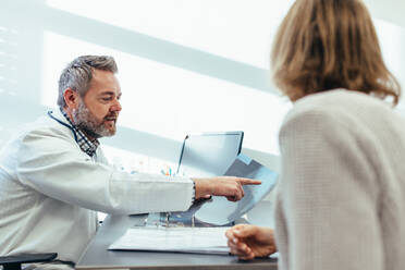 Medical specialist discussing medical scan results with female patient in his clinic. Doctor showing x-ray to patient in medical office. - JLPSF28050