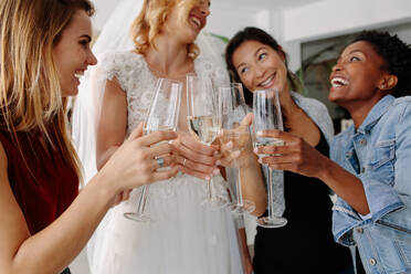 Frau im Brautkleid stößt mit Freunden mit Champagnergläsern an. Braut im eleganten Hochzeitskleid trinkt Champagner mit ihren Freunden in einem Brautmodengeschäft. - JLPSF28069