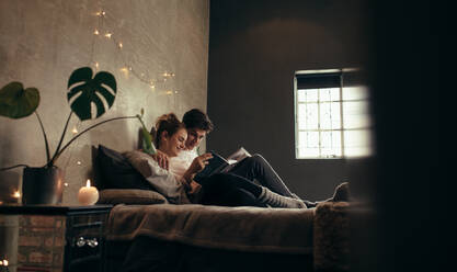 Junger Mann und Frau ruhen sich auf dem Bett mit einem Buch aus. Paar entspannt sich auf dem Bett und liest ein Buch. - JLPSF28102