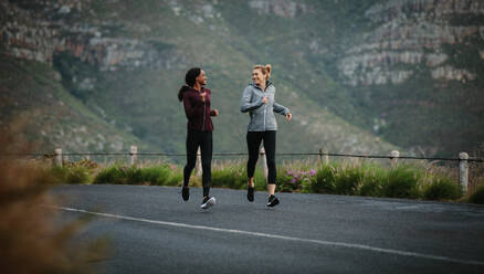 Frauen laufen auf der Straße früh am Morgen mit Hügeln im Hintergrund. Fitness Frauen joggen auf der Straße. - JLPSF28120