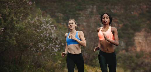 Zwei Frauen, die frühmorgens auf der Straße laufen, mit Hügeln im Hintergrund. Fitness-Frauen joggen auf der Straße. - JLPSF28138