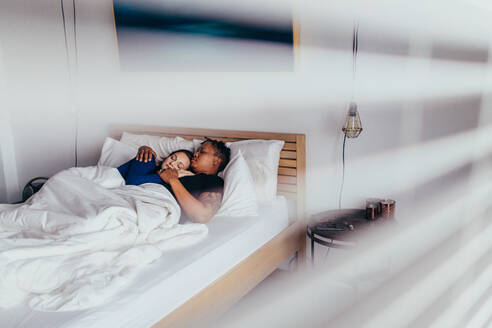 Interracial junges Paar umarmt, während auf dem Bett schlafen. Mann und Frau schlafen friedlich im Schlafzimmer. - JLPSF28143