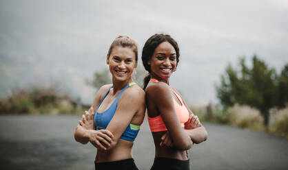 Young female runners standing back to back on mountain road - JLPSF28150