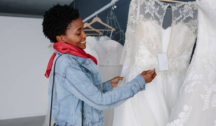 Lächelnd afrikanische Frau Einkaufen für Hochzeit Outfit in Braut Boutique. Braut Auswahl weißes Kleid im Geschäft der Hochzeit Mode. - JLPSF28174