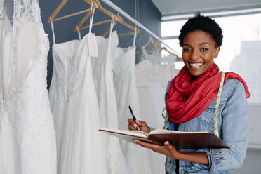 Porträt einer lächelnden Inhaberin eines Brautmodengeschäfts mit einem Tagebuch, die in ihrer Boutique arbeitet. - JLPSF28179