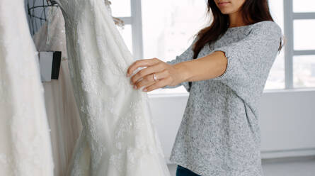 Junge Frau sieht sich in einer Boutique ausgestellte Brautkleider an. Fokus auf weibliche Hände, die ein Hochzeitskleid in einem Geschäft für Hochzeitsmode auswählen. - JLPSF28184