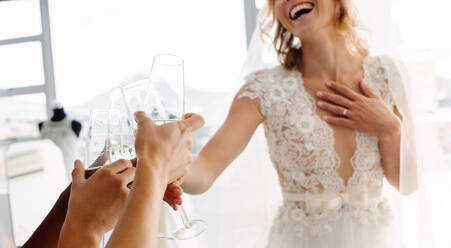 Ausschnitt einer Braut im Hochzeitskleid und ihrer Freundinnen, die in einer Brautboutique Champagner trinken; Fokus auf weibliche Hände, die in einem Geschäft für Hochzeitskleidung mit Champagner anstoßen. - JLPSF28209