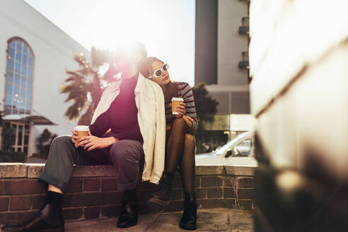 Mann und Frau sitzen mit einem Kaffee auf der Straße, ein Paar im Retro-Stil, das sich in der Stadt im Freien entspannt. - JLPSF28210