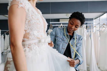 Professional wedding dress designer fitting bridal gown to woman in her store. Woman making adjustments to bridal gown in her boutique. - JLPSF28217