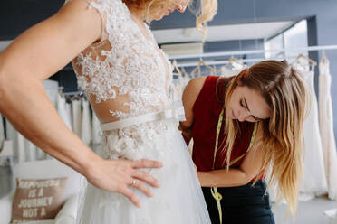 Geschickte Kleiderdesignerin bei der Anprobe des Brautkleides einer Frau in ihrer Boutique. Frau bei der Anpassung des Brautkleides im Atelier der Modedesignerin. - JLPSF28218