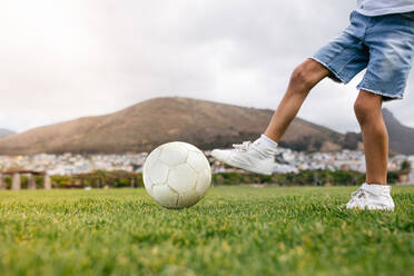 Nahaufnahme eines Jungen, der einen Fußball auf einem Spielplatz kickt. - JLPSF28250