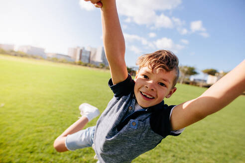 Close up of a boy jumping in air at a park. Cheerful boy enjoys being lifted in air while playing in a park. - JLPSF28257