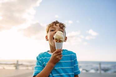 Junge isst ein Eis in der Nähe der Strandpromenade. Kleiner Junge im Urlaub, der sich ein Eis gönnt. - JLPSF28261